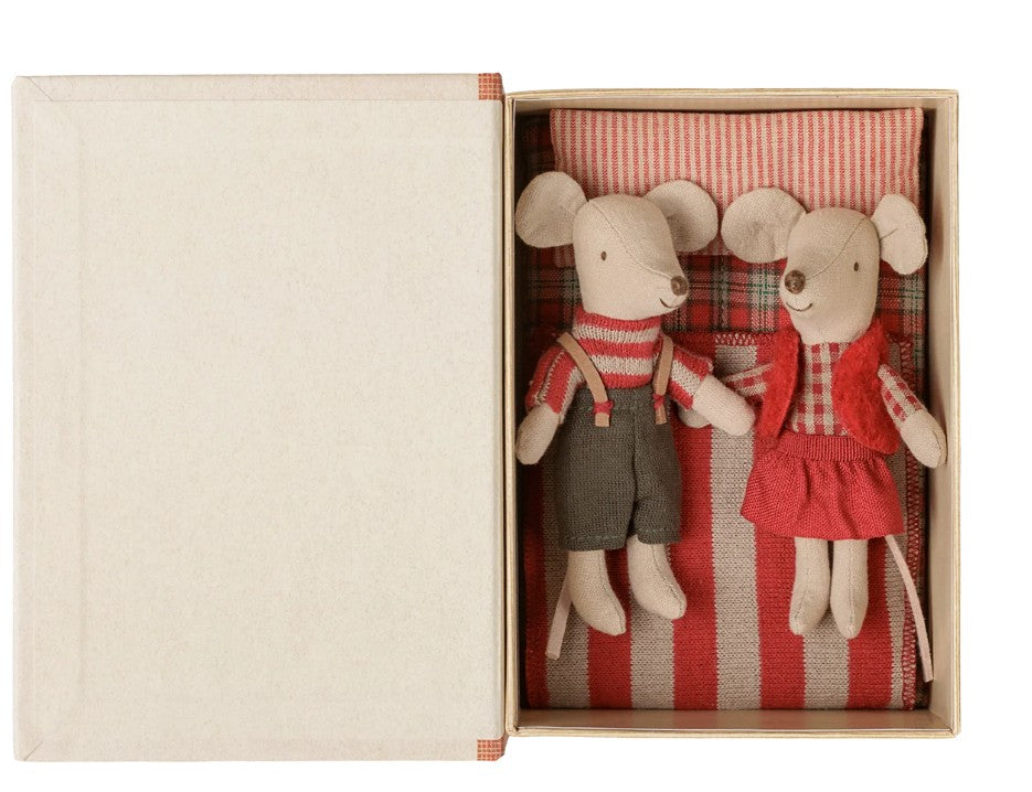 The Maileg Christmas twin mice, Little Sister and Brother in Book by Maileg lie side by side on a red-striped mattress inside an open cardboard box. Dressed in festive red and gray outfits, the pair comes with a matching pillow above their heads, making these adorable mice the perfect holiday gift.