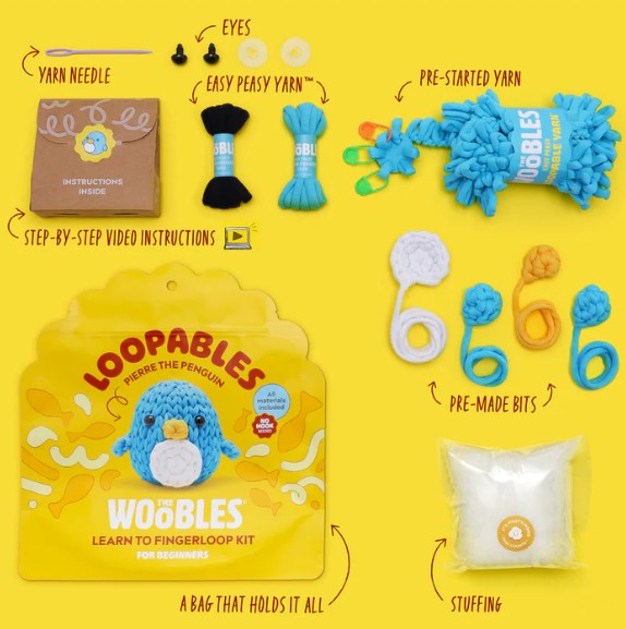 A flat lay of The Woobles Pierre the Penguin Loopables Kit displays a bag, yarn needle, eyes, yellow and blue yarn, instructions, pre-made yarn bits, stuffing, and pouch—ideal for beginner crafters.