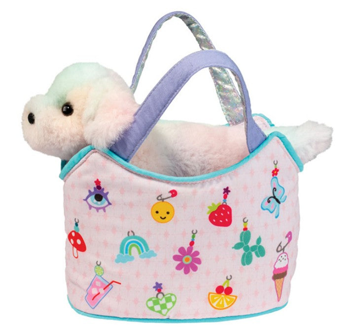 The Douglas Charmingly Yours Sassy Pet Sak features a plush white dog with pastel fur sitting in a light pink carry bag adorned with vibrant charms—like a smiley face, strawberry, rainbow, ice cream, butterfly, and flowers—for imaginative play.