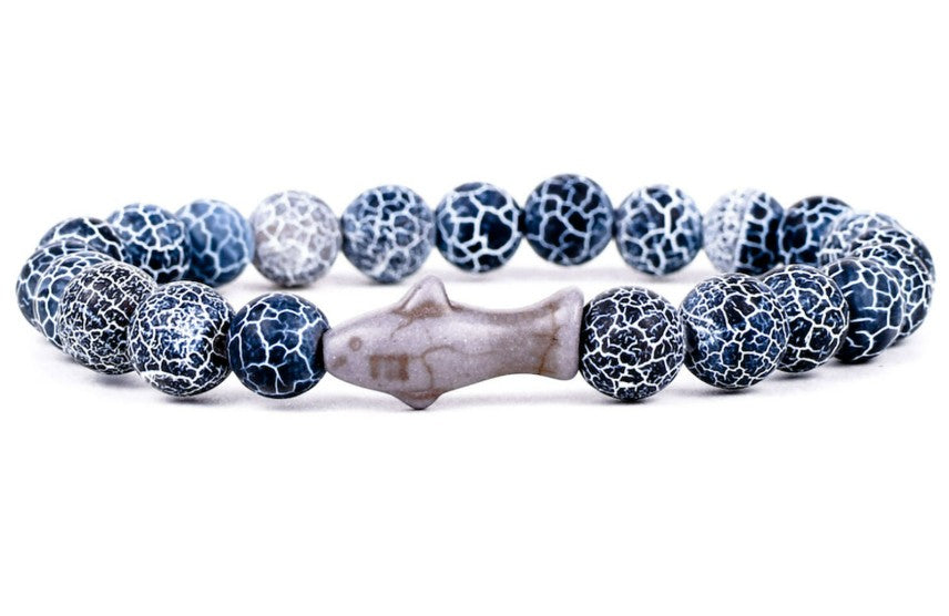 The fahlo Voyage - Deep Blue Shark bracelet features blue and white crackle-patterned beads and a central fish-shaped bead—perfect for marine wildlife conservation supporters or anyone interested in tracking sharks.