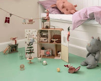 A children’s room featuring the Maileg SuitCasa playset with Little Sister and Brother Mouse from Maileg, surrounded by toy furniture, a plush pig on the bed, a plush rhino on the floor, and other toys. The Maileg miniature accessories and dolls are scattered across a mint green floor near a white bed and wall.