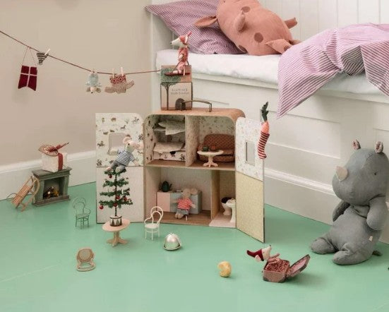 A children’s room featuring the Maileg SuitCasa playset with Little Sister and Brother Mouse from Maileg, surrounded by toy furniture, a plush pig on the bed, a plush rhino on the floor, and other toys. The Maileg miniature accessories and dolls are scattered across a mint green floor near a white bed and wall.