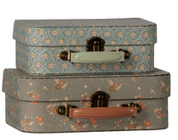 The Maileg Suitcase set, 2 pcs - Michette features two charming vintage-style suitcases stacked together—perfect for pretend play. The top suitcase is blue with a green handle and a decorative pattern, while the bottom one is brownish with a pink handle and small orange flowers. Both pieces showcase the whimsical design Maileg is known for.