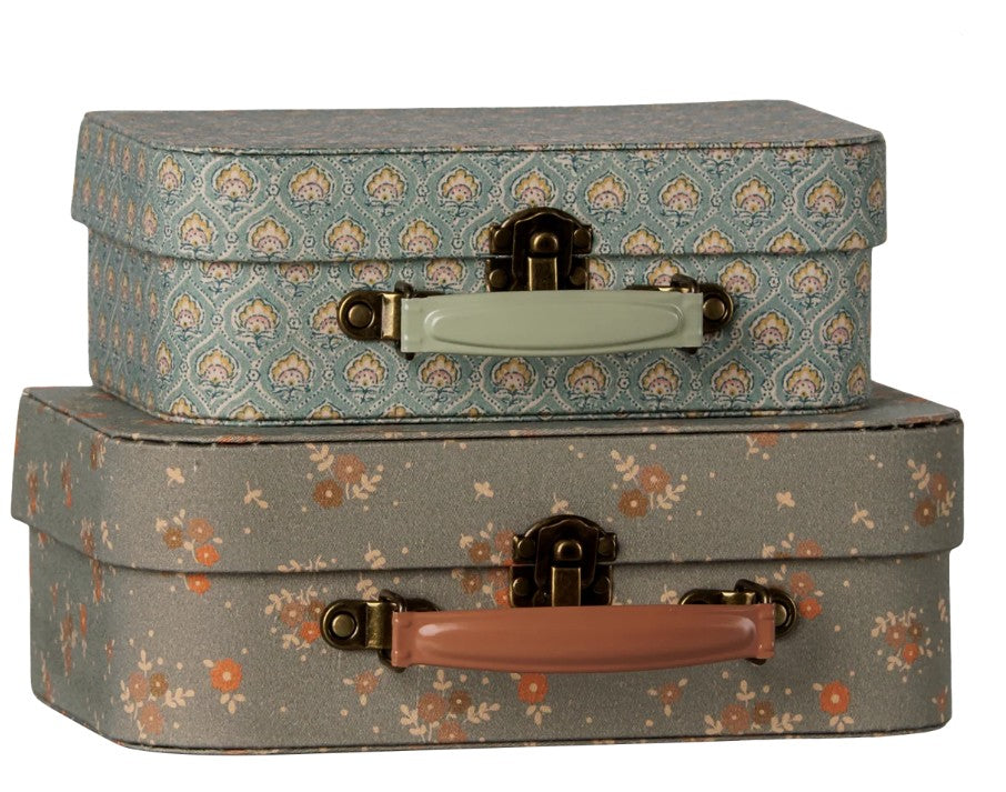 The Maileg Suitcase set, 2 pcs - Michette features two charming vintage-style suitcases stacked together—perfect for pretend play. The top suitcase is blue with a green handle and a decorative pattern, while the bottom one is brownish with a pink handle and small orange flowers. Both pieces showcase the whimsical design Maileg is known for.