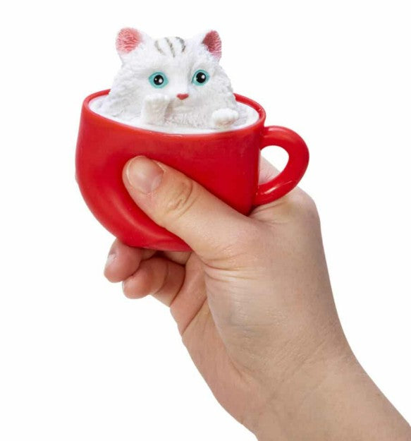 A hand holds a red cup with a cute white kitten figurine inside, peeking out with blue eyes and pink ears—the Pop-a-Chino Kittens by Schylling Toys, perfect as a cat fidget toy for stress relief and sensory play.