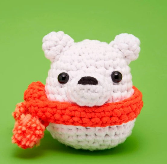 Lola Loca the Polar Bear Crochet Kit by The Woobles features a small crocheted bear with black button eyes, a black nose, and a chunky red scarf with pom-pom—perfect for beginners seeking an adorable project.