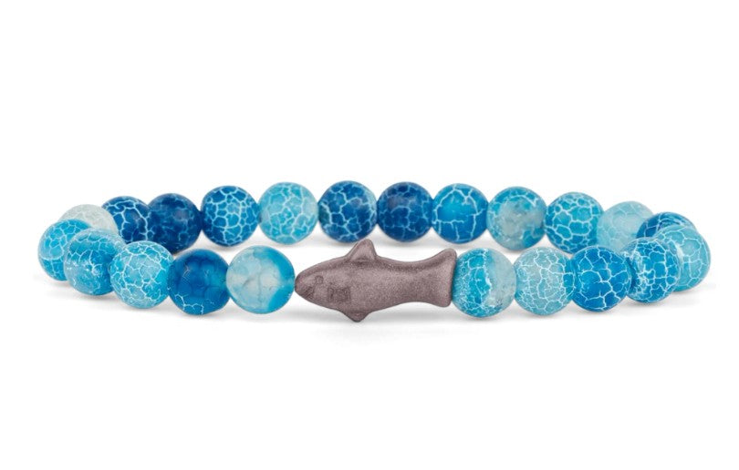The fahlo Voyage - Aqua Blue Shark bracelet features round blue and white marbled beads with a gray shark centerpiece, inspired by ocean conservation—perfect for marine life lovers.