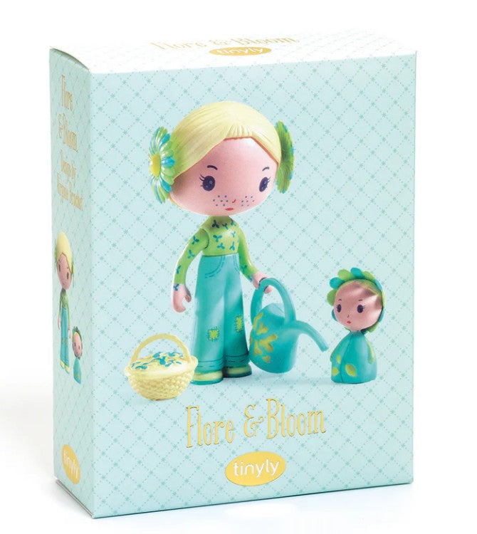 Showcasing the DJECO Tinyly Flore & Bloom set by DJECO, this box features a collectible figure of a blonde-haired girl doll dressed in teal pants, holding a watering can. She is accompanied by a small floral-inspired companion and a basket. The packaging has a light blue background with a subtle pattern.