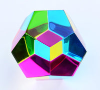 The Mundus by CMY Cubes is a shiny, multicolored geometric cube on a white background. Its reflective surfaces refract light into shifting pink, green, blue, and yellow hues.