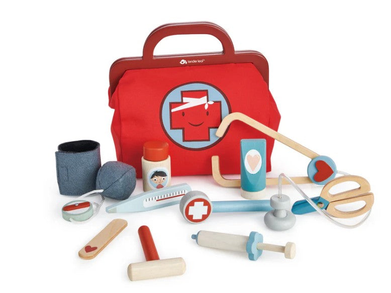 The Tenderleaf Doctors Bag is a red wooden bag with a white cross and smiling face, featuring child-sized play medical instruments like a stethoscope, syringe, thermometer, reflex hammer, ointment, and bandages for pretend play fun.