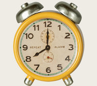 The Maileg Alarm Clock, Mouse - Yellow by Maileg is a vintage-style miniature clock with silver bells and legs, green edge detailing, black numbers, and shows 7:00—perfect for dollhouse décor.