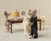 The Maileg Wedding Mice Couple In Box, Mum And Dad by Maileg features plush bride and groom mice dancing, with another mouse in a purple dress by a tall cake and empty gold chair—ideal for display or as a charming keepsake box.