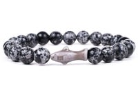The Voyage - Ocelli Stone Shark bracelet by fahlo features black and gray speckled beads with a central shark-shaped bead, perfect for ocean conservation enthusiasts. Displayed on a white background.