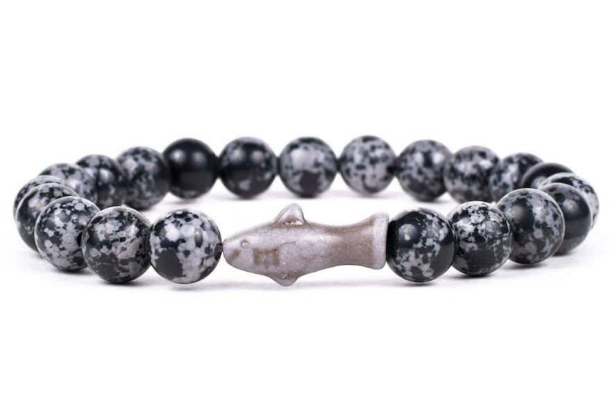 The Voyage - Ocelli Stone Shark bracelet by fahlo features black and gray speckled beads with a central shark-shaped bead, perfect for ocean conservation enthusiasts. Displayed on a white background.