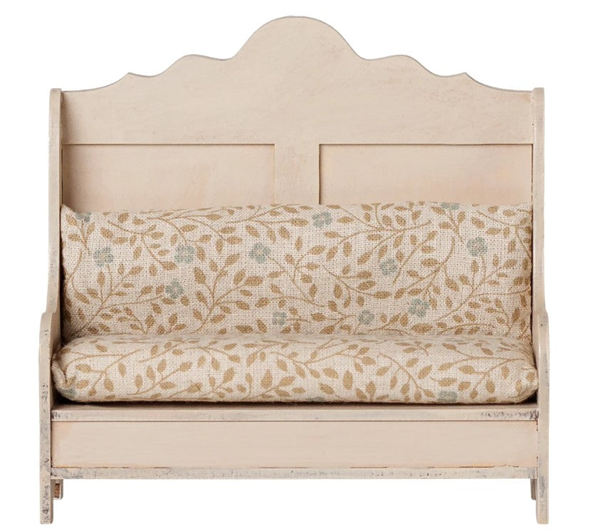 The Maileg Kitchen Bench, Mouse - Light Sand by Maileg features a cream-colored wooden frame with decorative backrest and armrests. It comes with a beige cushion adorned with a subtle leaf and berry pattern in muted tones, giving it a rustic, vintage charm—perfectly sized for Maileg mice to enjoy their miniature meals in style.