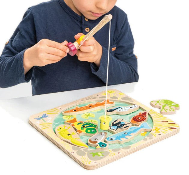A child plays Pond Dipping by Tenderleaf, using a magnetic fishing rod to catch colorful wooden pond creatures from a pond-themed play set.
