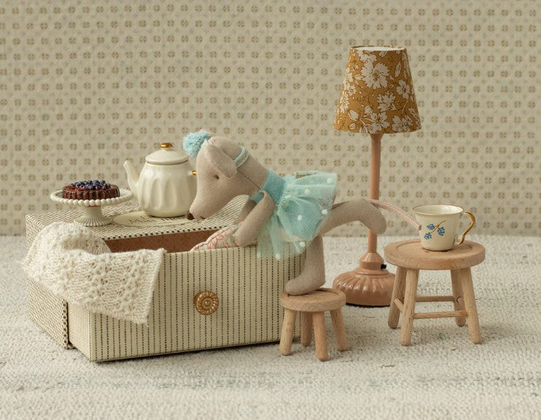 The Maileg Dance Mouse In Daybed, Little Sister by Maileg lounges in a striped box with miniature furniture—lamp, cake, stools, and daybed—inviting imaginative play against a charming patterned background.