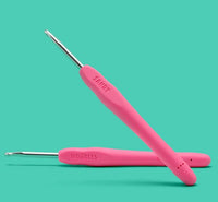 Two pink crochet hooks with metal tips and ergonomic soft-grip handles, included in The Woobles Sandy the Watermelon Crochet Kit, rest on a teal background—perfect for beginners or expanding your crochet kit.