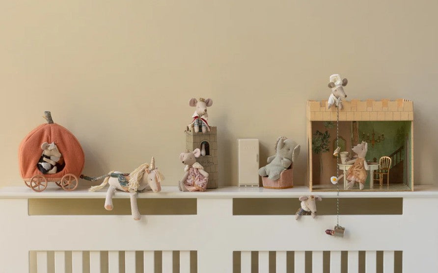 Stuffed mice and animals are arranged on a white shelf, sitting on toy furniture and props—including a pumpkin carriage, a unicorn, the charming Maileg Castle Hall playset by Maileg, and a pull-up swing—decorated with delightful Maileg mouse accessories against a beige wall.