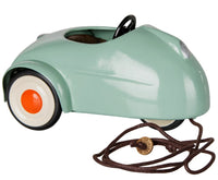 A small, light mint Maileg Car, Mouse with white wheels featuring orange centers, a steering wheel, and a brown pull string with a wooden tag attached—perfect for miniature car collections or as an adorable addition to your Maileg mice toys set.