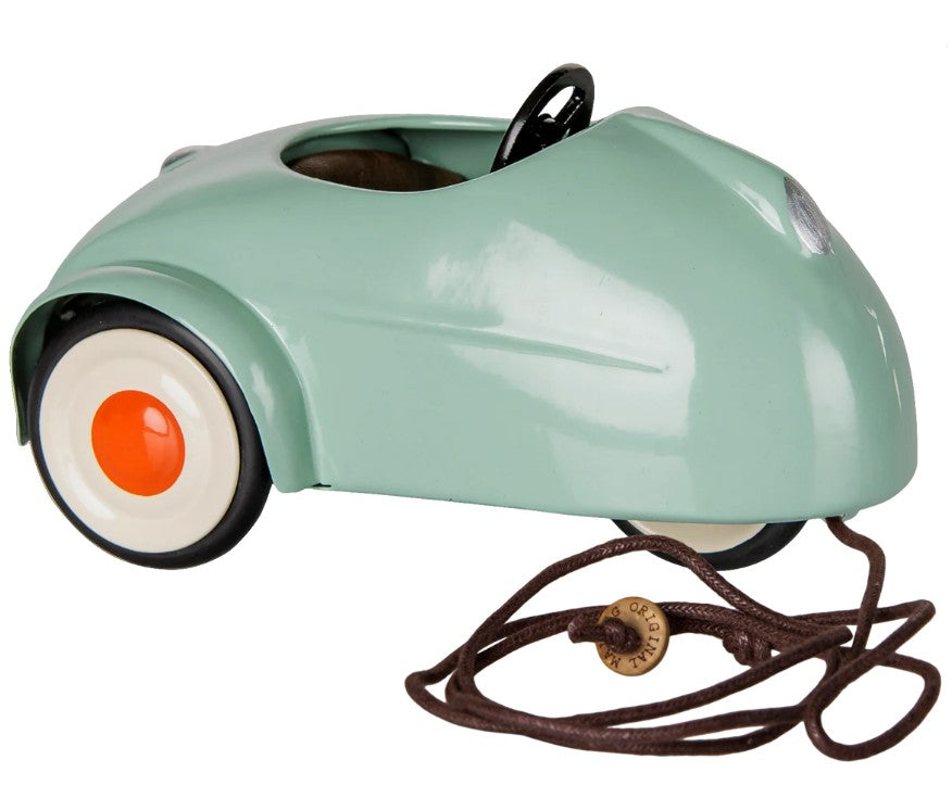 A small, light mint Maileg Car, Mouse with white wheels featuring orange centers, a steering wheel, and a brown pull string with a wooden tag attached—perfect for miniature car collections or as an adorable addition to your Maileg mice toys set.