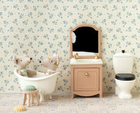 Two stuffed animals sit in a tiny dollhouse bathroom featuring Maileg Mouse furniture, including the Maileg Toilet, Mouse by Maileg, a vanity with mirror, patterned floor, and floral wallpaper for a playful scene.