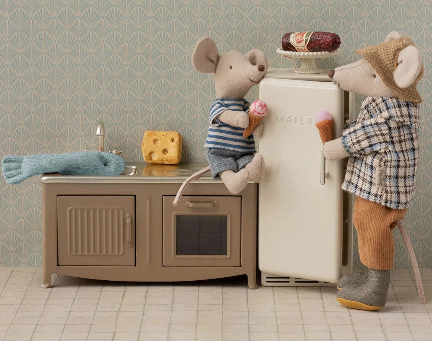 Maileg Granddad Mouse by Maileg stands in a playful miniature kitchen, enjoying an ice cream cone beside a toy fish and cheese. Another mouse is near a white fridge topped with cake, adding whimsy to the charming scene.