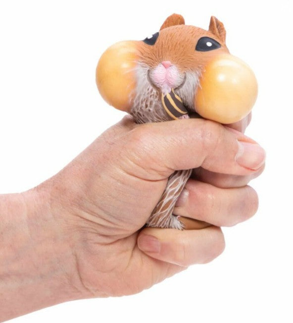 A hand squeezes the Schylling Toys Chonky Cheeks Hamster, a sensory toy with big cheeks, a pink nose, and black eyes designed for stress relief.