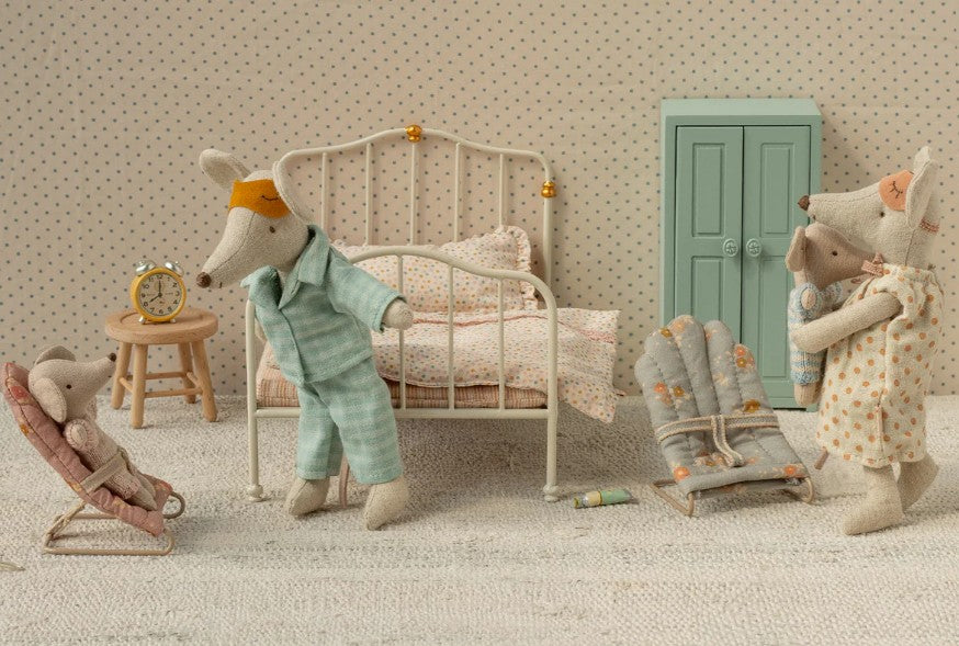 Three Maileg My-sized mice are in a pastel bedroom: one wears pajamas and an eye mask, one holds a baby mouse, and the baby sits in the Maileg Babysitter, My - Rose. The room includes a bed, wardrobe, and soft decor.