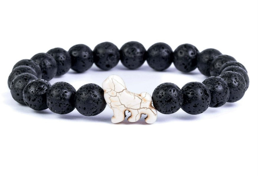 The fahlo Excursion - Lava Stone Lion bracelet is crafted from round black lava stones with a single white bead shaped like a lion, symbolizing conservation efforts, and is beautifully displayed on a white background.