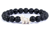 The fahlo Excursion - Lava Stone Lion bracelet is crafted from round black lava stones with a single white bead shaped like a lion, symbolizing conservation efforts, and is beautifully displayed on a white background.