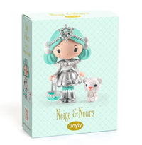 Box for DJECO Tinyly Neige & Nours by DJECO. It features a collectible figure with teal hair and a silver outfit holding a basket, standing beside a small white bear. The light blue background with a subtle diamond pattern complements the winter-inspired design.