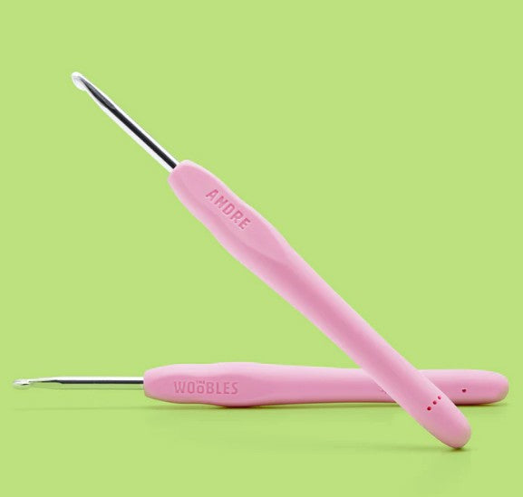 Two pink-handled crochet hooks from The Woobles’ Andre the Skunk Pink Crochet Kit are shown on a light green background. Both feature ergonomic handles and metal tips—perfect for beginner-friendly crochet.