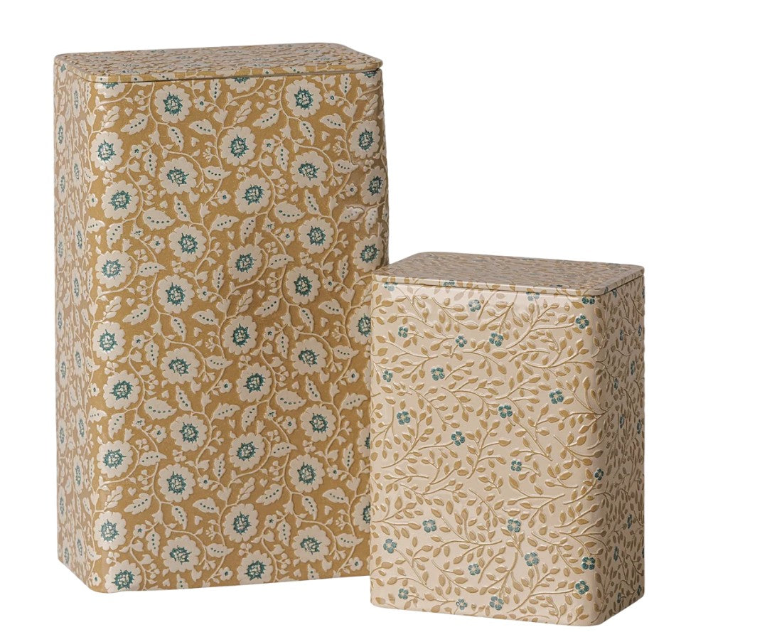 A set of two rectangular Maileg metal boxes with tight-fitting lids, featuring ocher and blue floral designs. This Maileg Metal box set - Flowers - Ocher/Blue (2 pcs) combines style and practicality, with the taller tin placed behind and to the left of the shorter one.