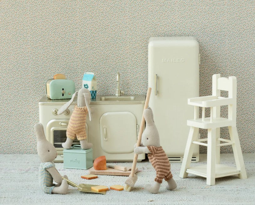 Three stuffed bunny toys in striped outfits play in a vintage miniature kitchen featuring Maileg Mouse furniture, adorable accessories, and the Maileg Bread Box W. Utensils, Miniature by Maileg among items like a fridge, stove, sink, toaster, and white high chair.