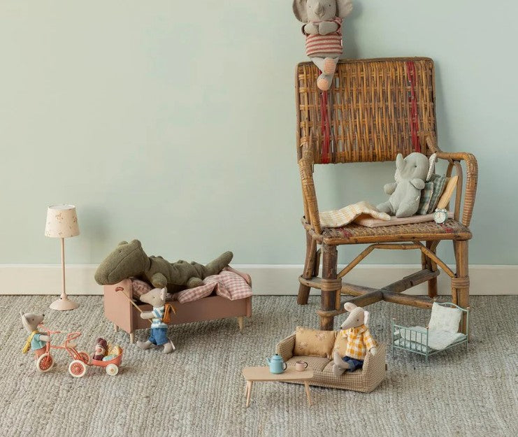 A cozy playroom with stuffed animal mice and elephants in Maileg Mouse furniture: a wicker chair, bed, lamp, couch, tricycles, a tiny shopping cart, and the Maileg Coffee Table, Mouse - Nature by Maileg topped with a tea set.