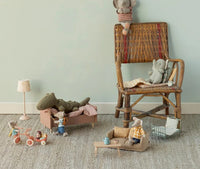 A cozy playroom with stuffed animal mice and elephants in Maileg Mouse furniture: a wicker chair, bed, lamp, couch, tricycles, a tiny shopping cart, and the Maileg Coffee Table, Mouse - Nature by Maileg topped with a tea set.