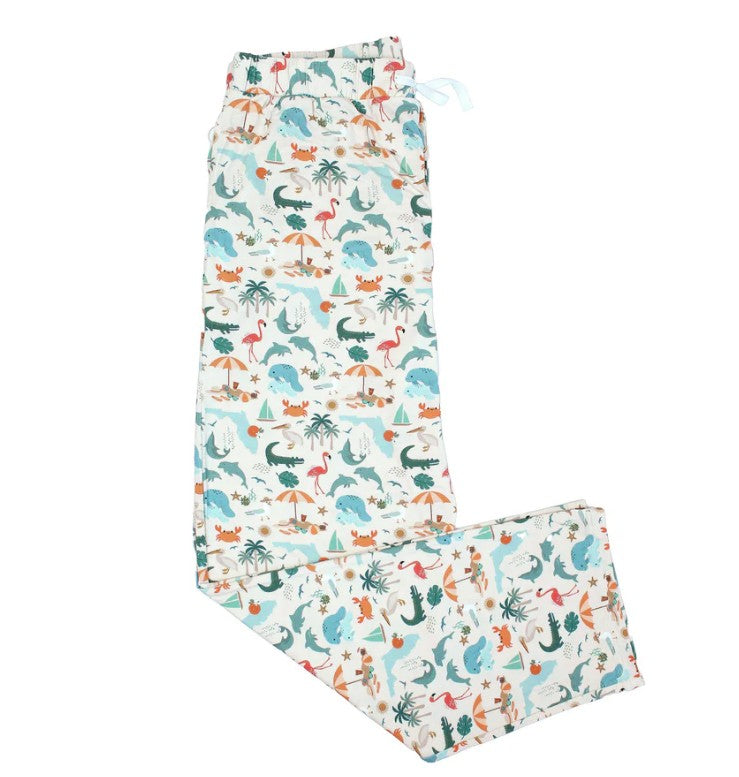The Emerson & Friends Explore Florida Souvenir Bamboo Adult Pajamas Lounge Pants in Beige/Multi feature a playful, colorful print of various dinosaurs, trees, and plants in blue, green, orange, and pink tones. Crafted from ultra-soft bamboo fabric for ultimate comfort, these lounge pants are displayed laid flat with one leg folded over.