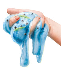 A hand holds So Slime Stinky Slime by License 2 Play—a stretchy blue slime infused with shiny black beads and small green worm-like shapes, perfect for sensory play and surprise scents.