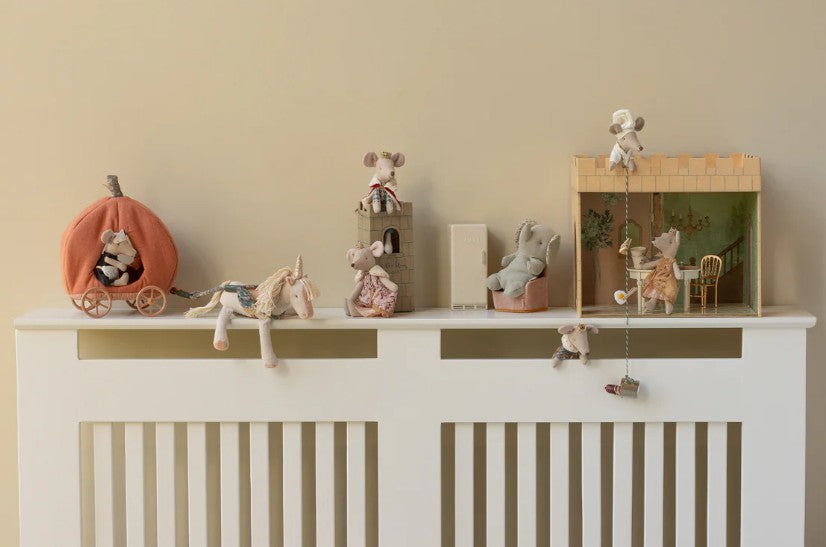 A shelf displays Maileg plush mice in assorted costumes, the Maileg Pumpkin Carriage, a unicorn, castle, and toy theater—ideal for imaginative storytelling—all set against a beige wall.