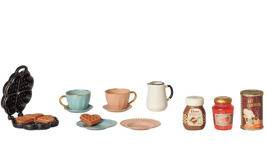 The Maileg Waffle Set, Mouse by Maileg is a charming miniature breakfast set designed for pretend play with Maileg mice. It includes a toy waffle maker, waffles, two cups with saucers, a small plate, a white pitcher, jars of spread, a can of hot chocolate, and a jar of strawberry jam—all beautifully arranged in a row.