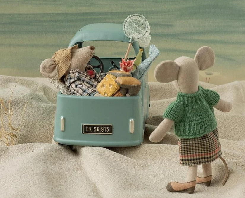 Two Maileg toy mice—including the Maileg Grandma Mouse, dressed in a green sweater and plaid skirt—are on a playful adventure in the sand: one mouse drives a car packed with cheese and fishing gear while Grandma Mouse stands cheerfully outside, ready for imaginative fun from the beloved Maileg brand.