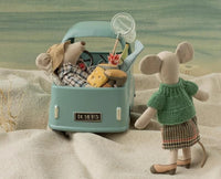 Two Maileg toy mice—including the Maileg Grandma Mouse, dressed in a green sweater and plaid skirt—are on a playful adventure in the sand: one mouse drives a car packed with cheese and fishing gear while Grandma Mouse stands cheerfully outside, ready for imaginative fun from the beloved Maileg brand.
