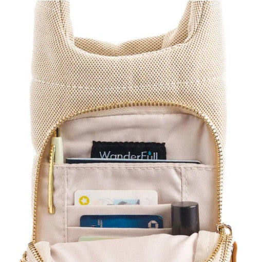 The HydroBag Handle Oatmeal Canvas by Wader Full Brand is a beige fabric bag with a gold zipper, partially open to show cards, a tube, and an interior pocket featuring a tag that reads “WanderFull.” This versatile hydration bag accessory offers an organized interior with sections for various items.