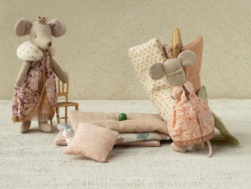 Maileg's Princess And The Pea, Big Sister Mouse features a charming mouse dressed in patterned clothes, resting on blankets with a green pea beneath—a whimsical tribute to the classic fairy tale.