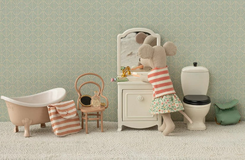 Maileg Tricycle Mouse, Big Sister - Green by Maileg features Big Sister in a striped top and floral skirt with a tricycle, purse, and bathroom set—complete with vanity, bathtub, toilet, chair, towel—all on a textured floor for imaginative play.