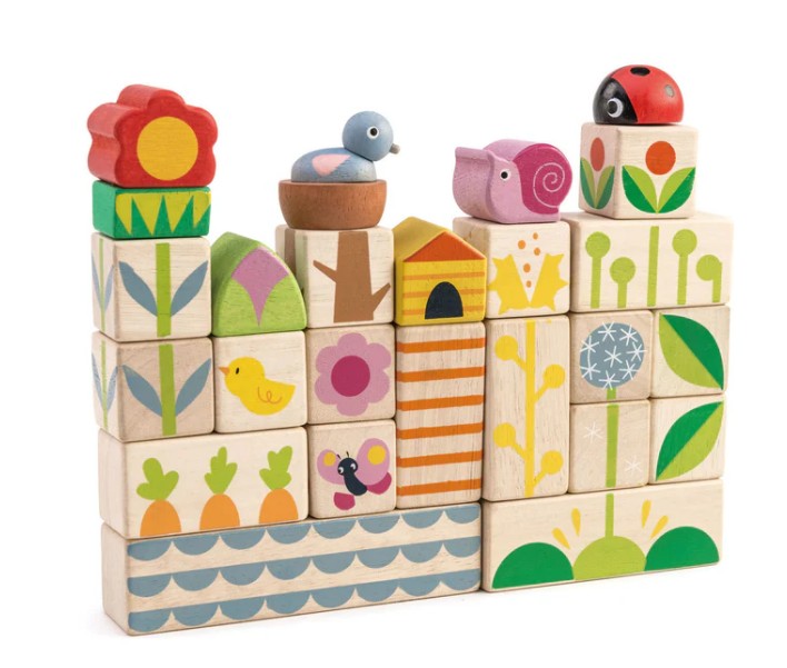 Tenderleaf Garden Blocks are stacked to create a playful garden scene with flowers, birds, a ladybug, and nature patterns. Some wooden blocks feature carrots, leaves, and geometric designs for imaginative play.