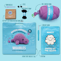 The Woobles Phyllis the Manatee Extra Squeezy Crochet Kit includes pre-started purple yarn, a crochet hook, stuffing, yarn needle, eyes, step-by-step instructions, and a bag with an illustrated purple manatee on the front.