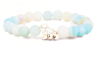 The Excursion - Sky Stone Lion bracelet by fahlo features pastel blue and white beads with a white and gold marbled lion charm, inspired by animal tracking for wildlife conservation.