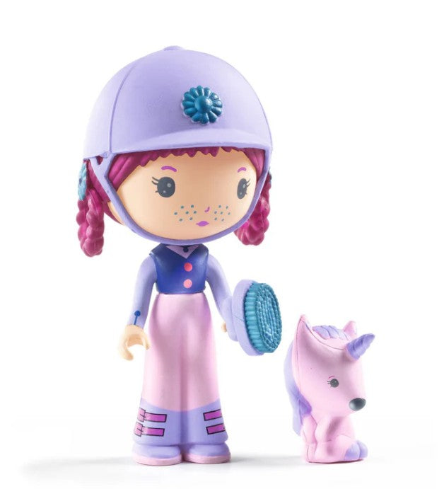 The DJECO Tinyly Joe & Gala collectible figure set by DJECO features a toy doll with purple braided hair, dressed in a lavender helmet and dress, standing beside a small, pastel purple unicorn miniature. Both figures showcase an adorable, cartoon-like design on a white background.